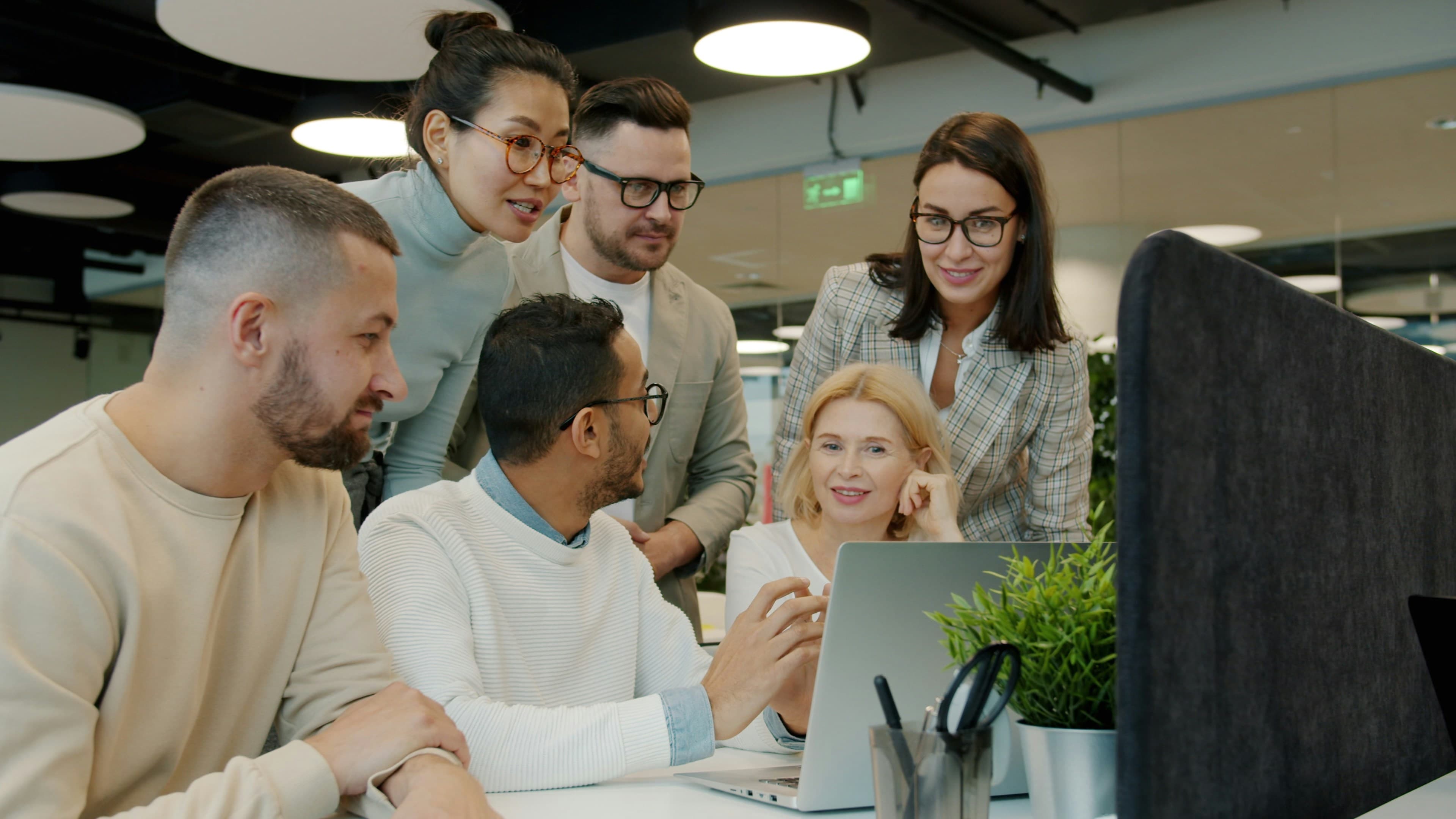 Equipe de profissionais conversando em torno de um notebook em ambiente corporativo